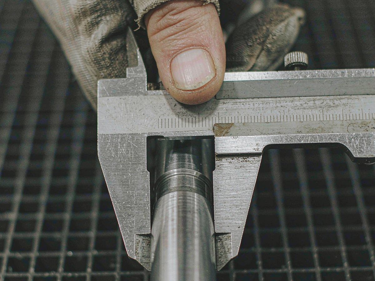 Gloved hands measuring a bolt shank with a vernier caliper